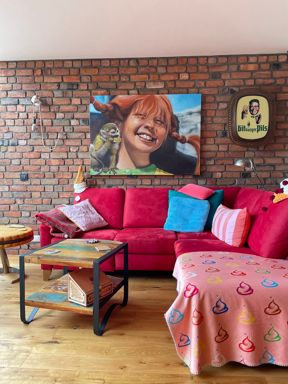 Farbenfrohes Wohnzimmer mit rotem Sofa und Ziegelwand aus recycelten Altziegeln, kombiniert mit Pop-Art und Retro-Elementen – kreative Wandgestaltung mit Charakter