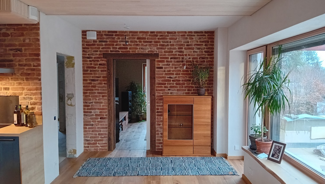 Gemütliches Wohnzimmer mit rustikaler Wandverkleidung aus recycelten Ziegeln und modernen Holzmöbeln. Die Ziegelstruktur verleiht dem Raum eine natürliche Wärme und sorgt für eine einladende Atmosphäre