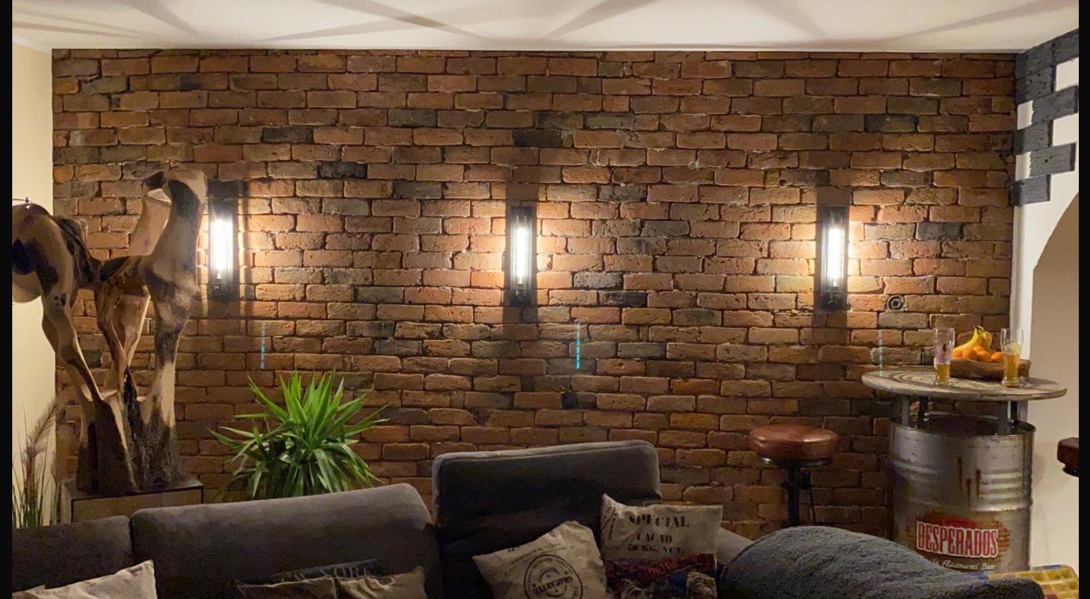 Wohnzimmer mit stimmungsvoll beleuchteter Ziegelwand, gefertigt aus recycelten Altziegeln – authentischer Industrial-Look mit viel Atmosphäre
